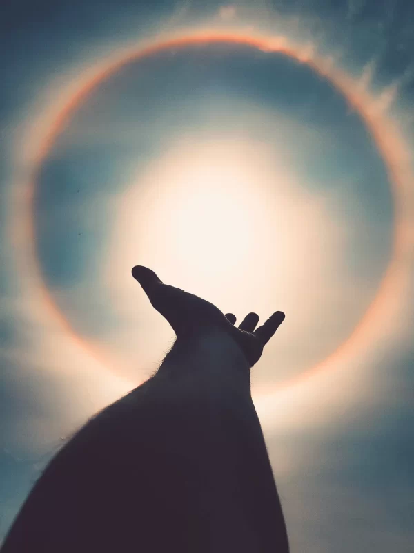 Alt tag: A person's hand reaching towards a rainbow circle in the sky, symbolizing past life regression and spiritual exploration.